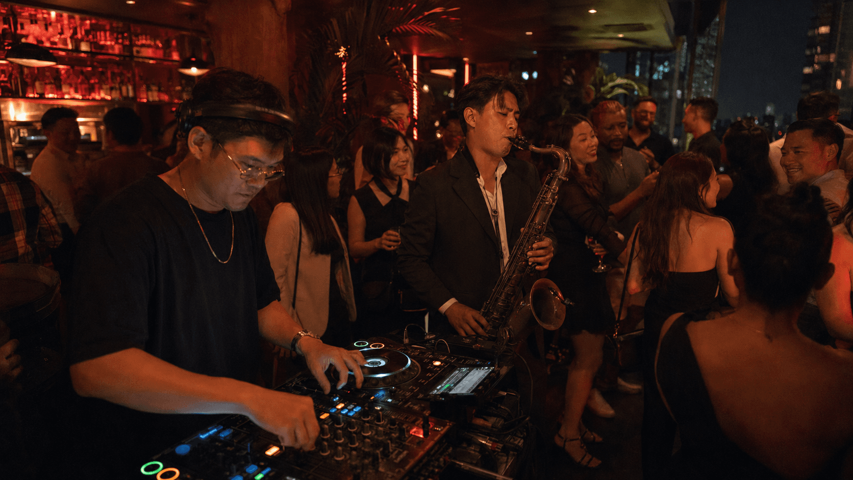 DJ and saxophonist performing during a busy rooftop event.